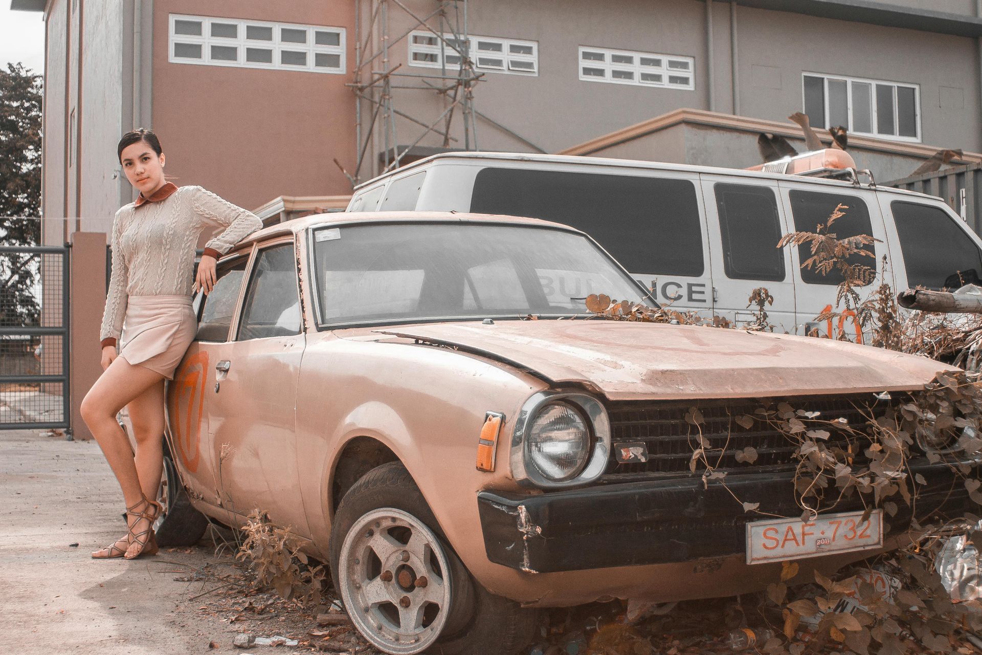 A woman is standing next to an old rusty car.