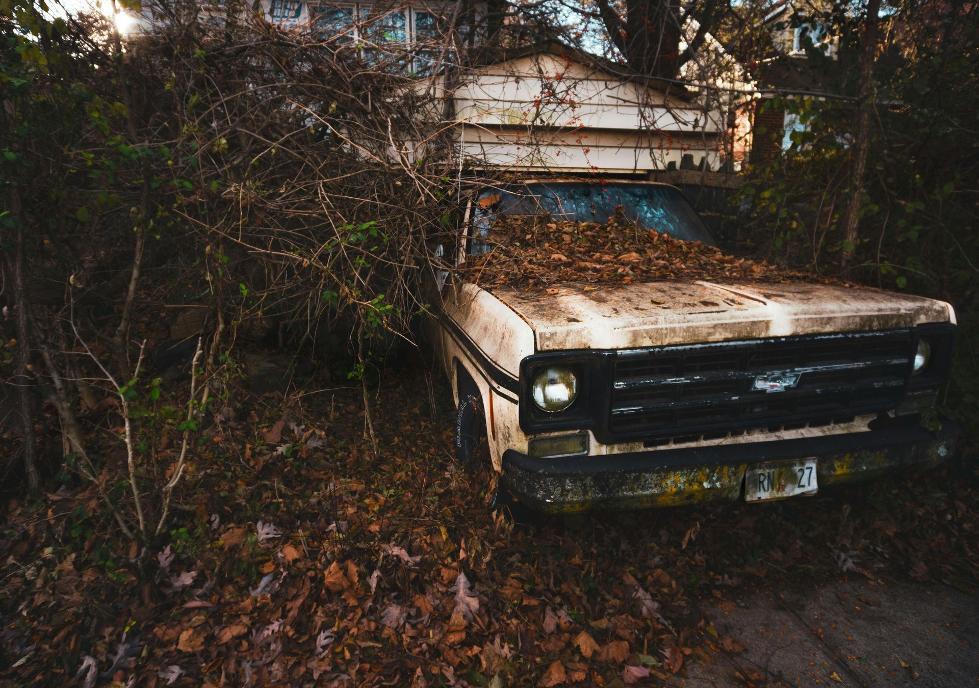 An old truck is covered in leaves in a yard.