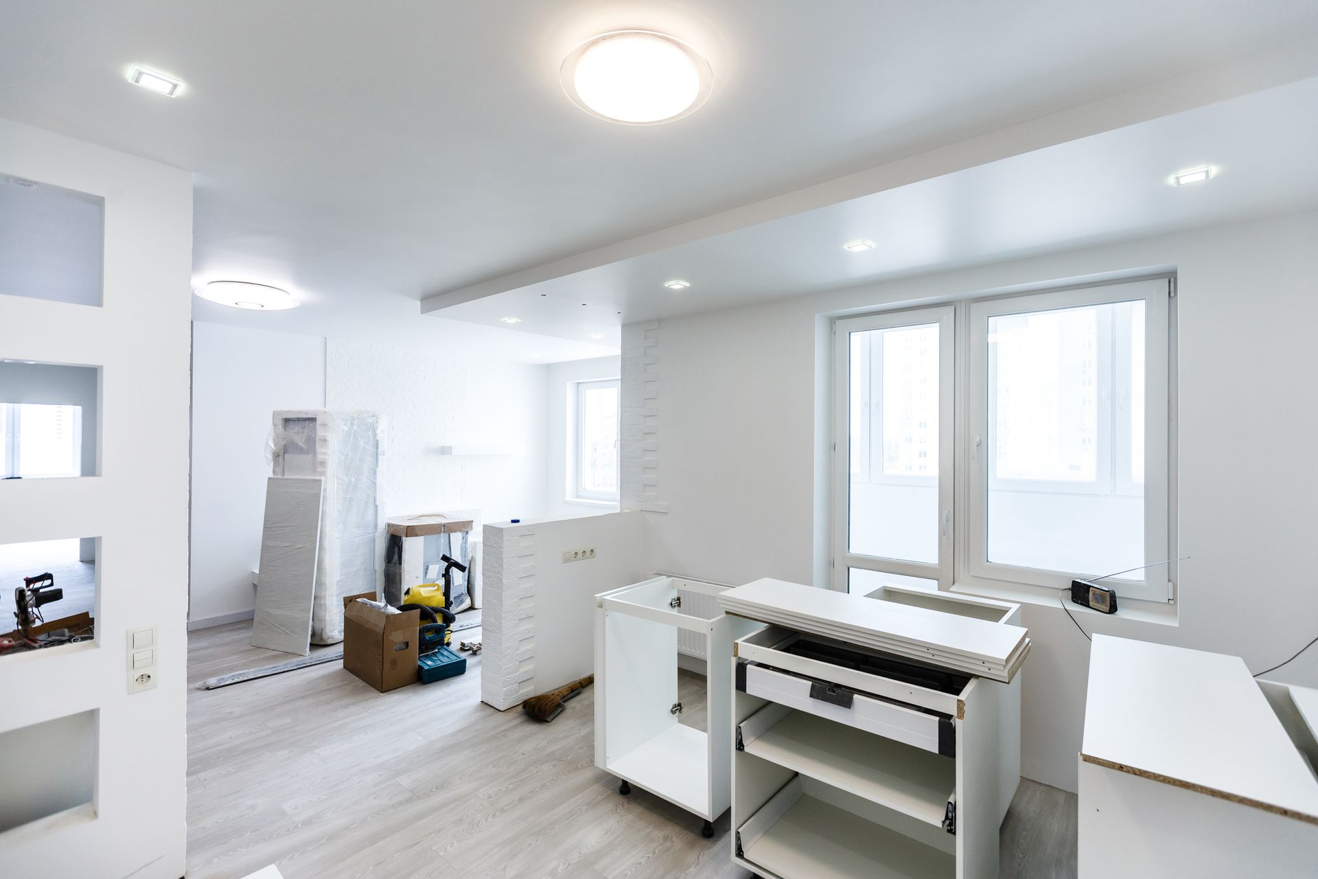 Renovated white room with unfinished cabinets, tools, and construction materials.
