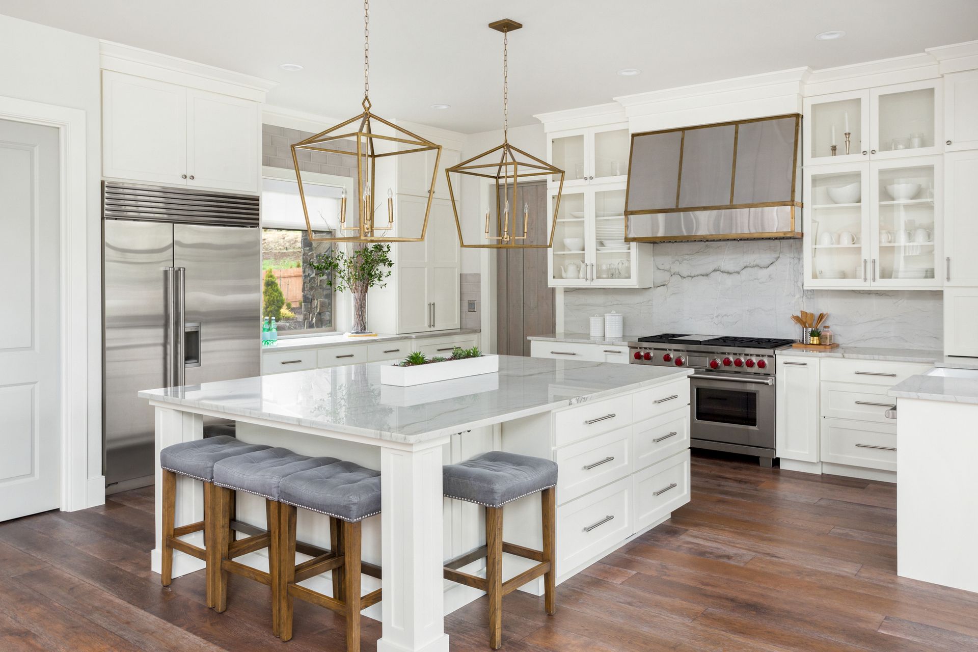 Bright white kitchen with a large island, stools, and stainless steel appliances.