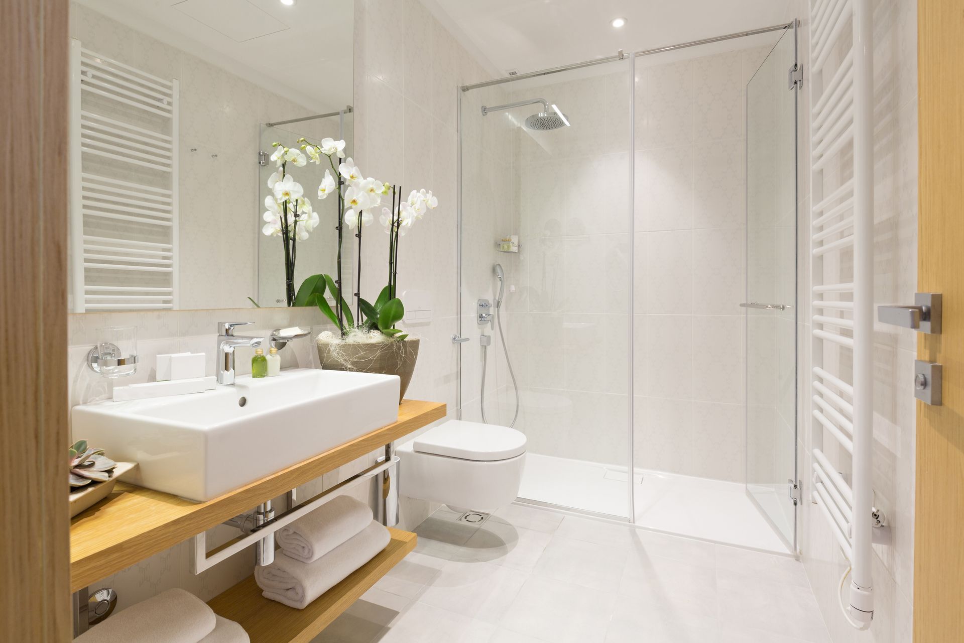 Modern white bathroom with glass shower, white sink, and towel rack.