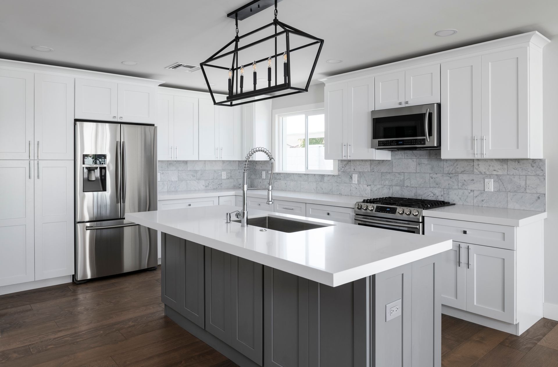 Modern kitchen with white cabinets, grey island, stainless steel appliances, and hardwood floors.