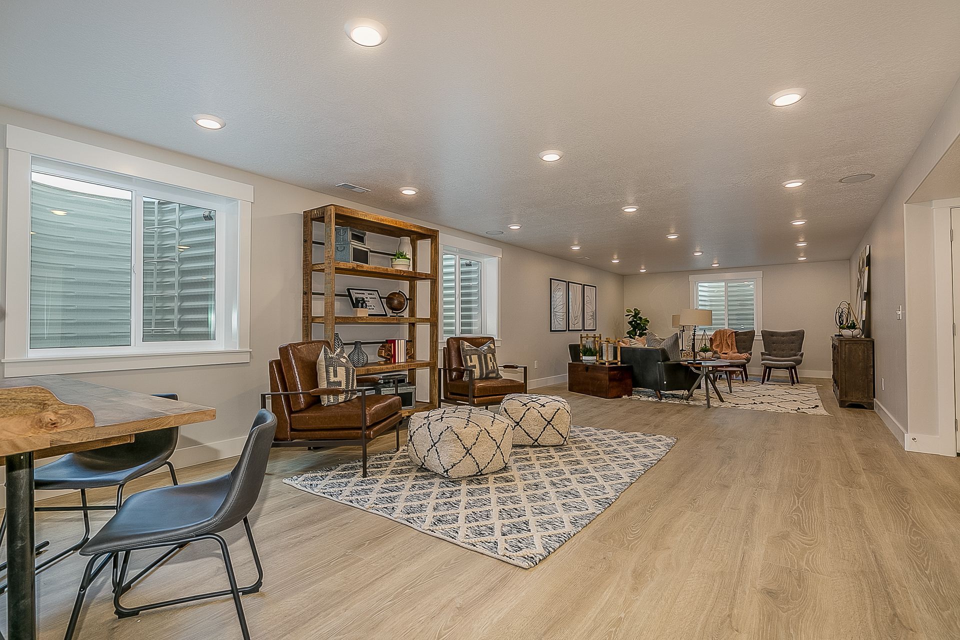 Spacious, well-lit basement living area with furniture, rug, and bookshelf. Neutral tones, recessed lighting, and a window.