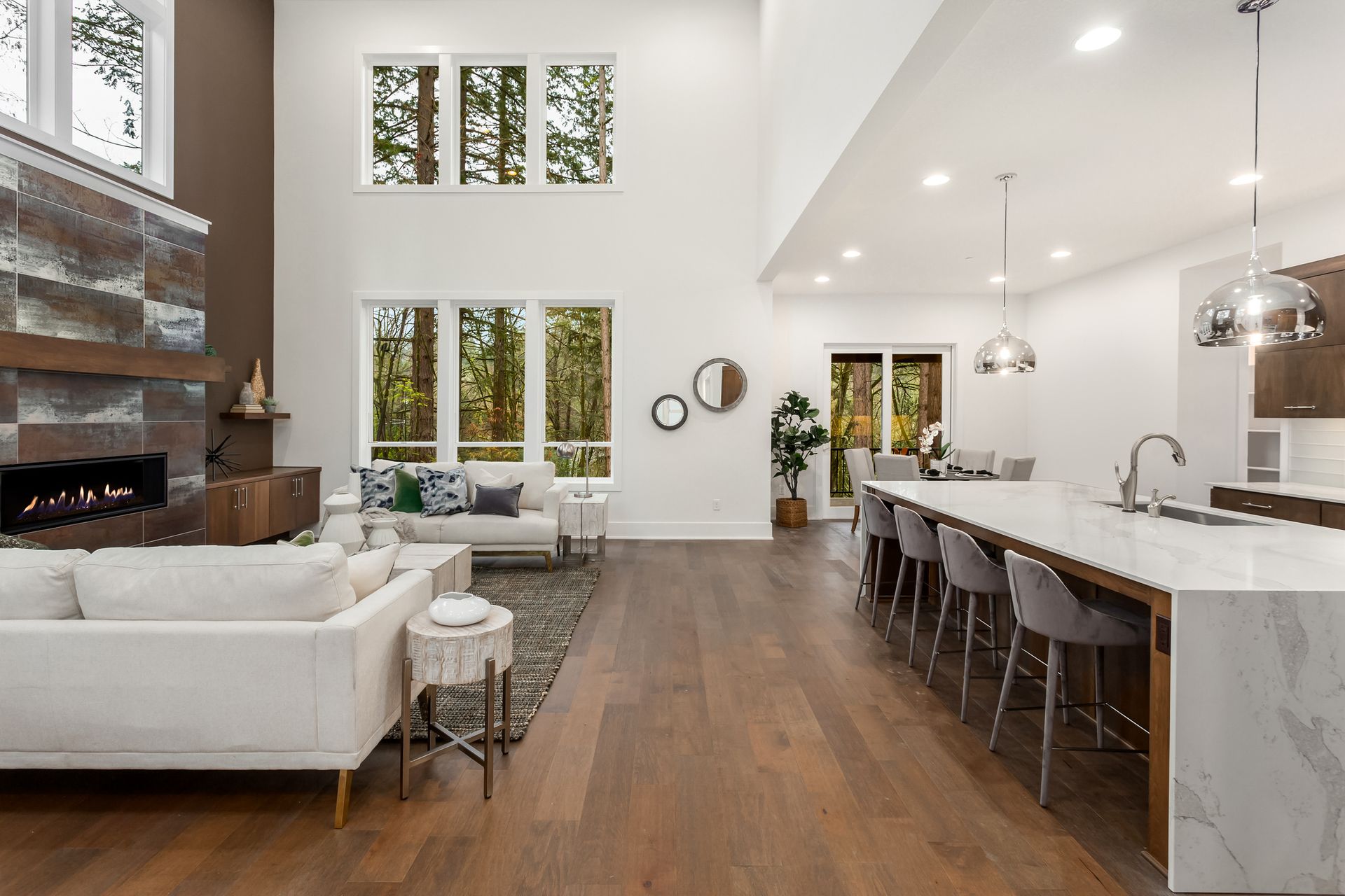 Spacious, modern living room with white walls, fireplace, and kitchen island; hardwood floors.