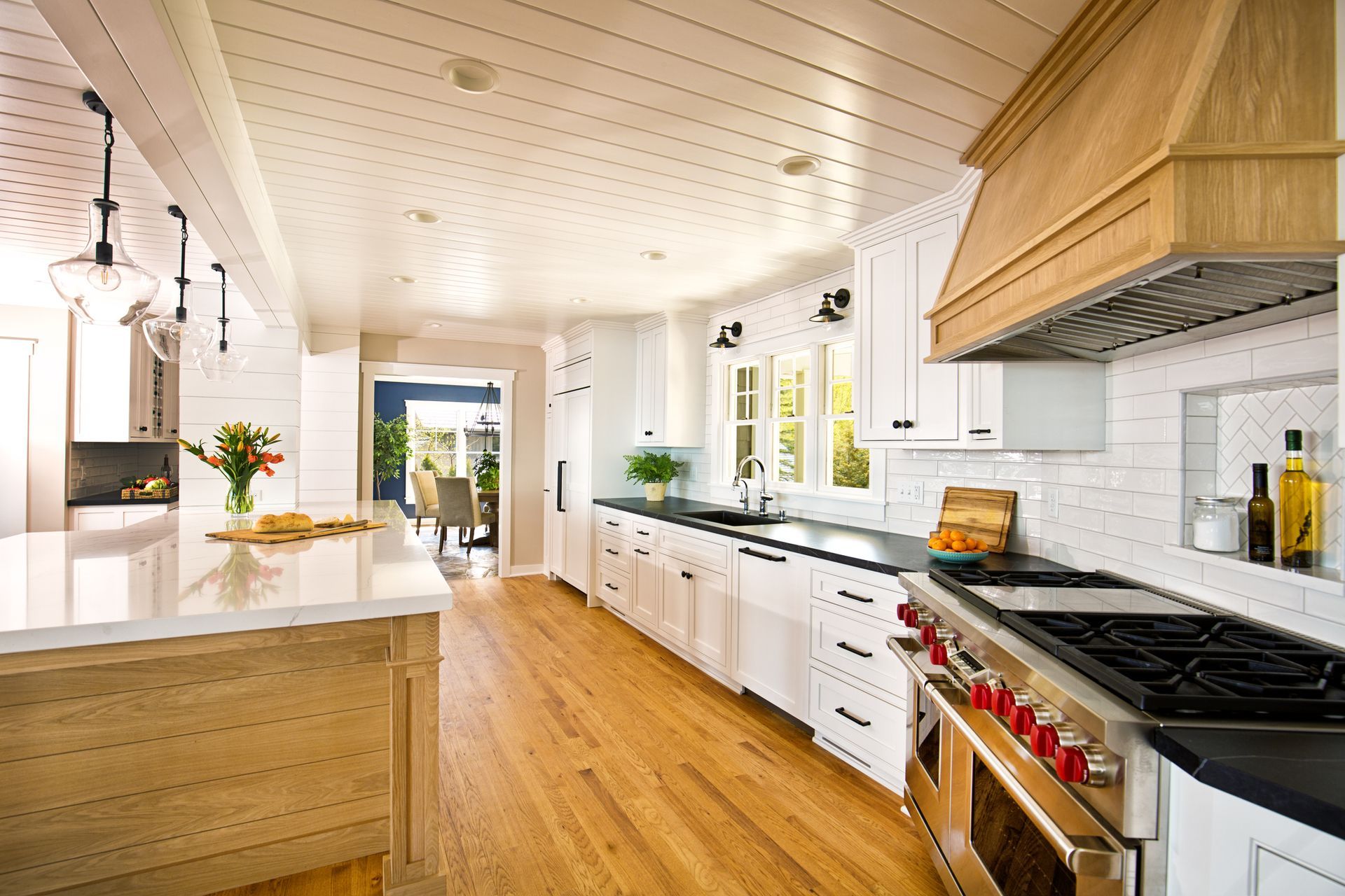 Light-filled kitchen with white cabinets, wooden floor, island, and stainless steel appliances.