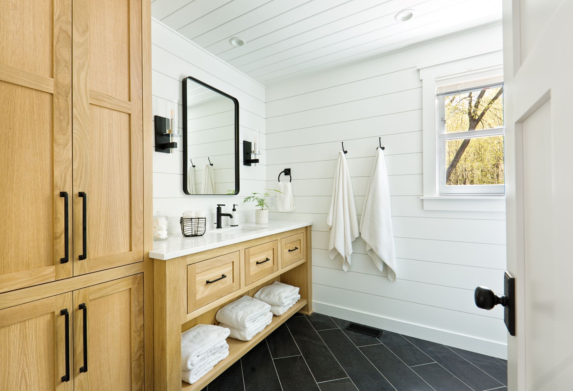 Bathroom with light wood cabinetry, white walls, and black fixtures.