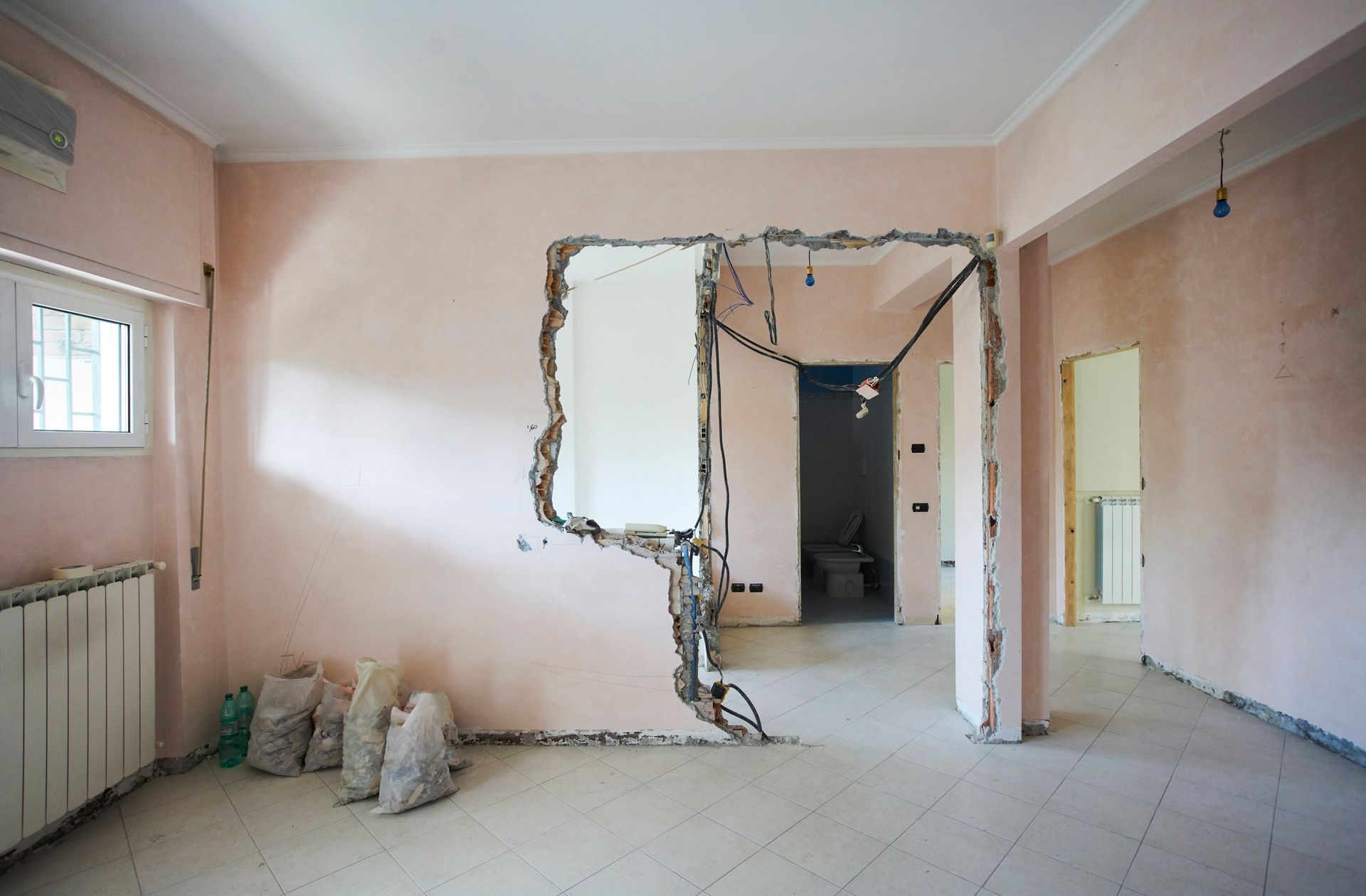 Room in renovation, pink walls, new doorway, wires exposed, bags of debris, tile floor.