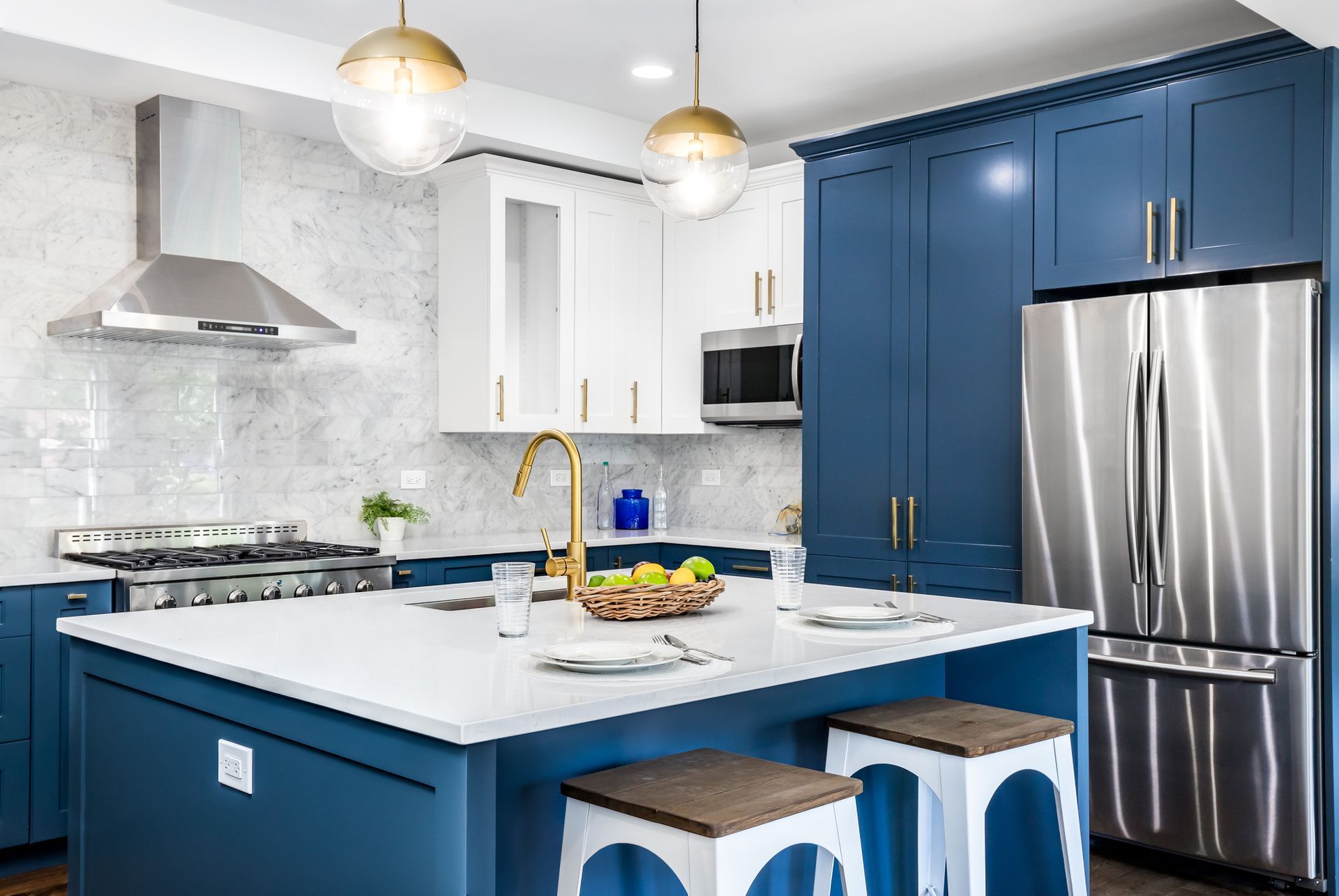 Blue and white kitchen with island, stainless steel appliances, gold accents, and two stools.