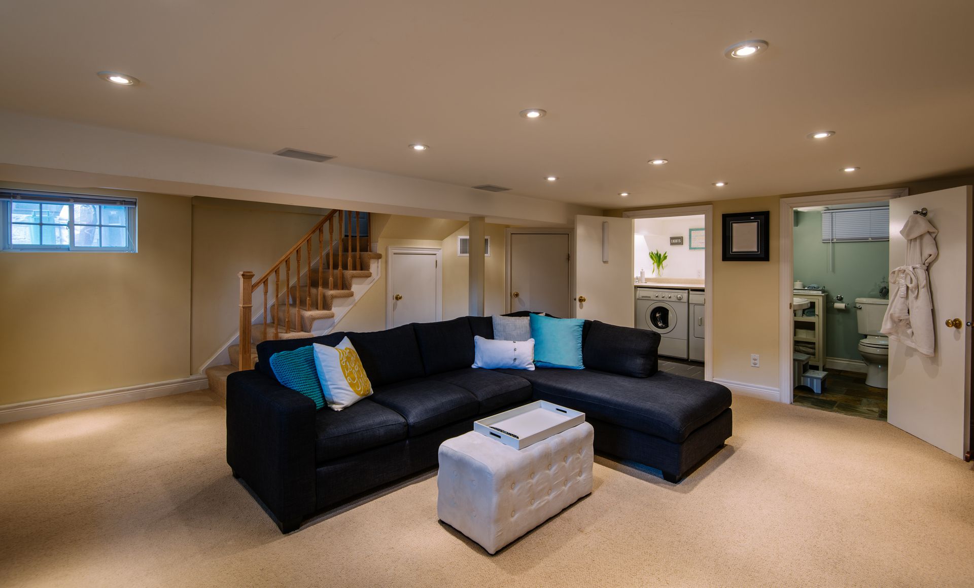 Black sectional sofa and ottoman in a finished basement. Beige walls and carpet.