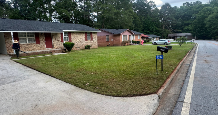 A brick house with a red door and a freshly mowed lawn next to a suburban street.