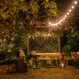 An outdoor patio decorated with string lights, Christmas trees, and a cozy bench, creating a warm, festive atmosphere.