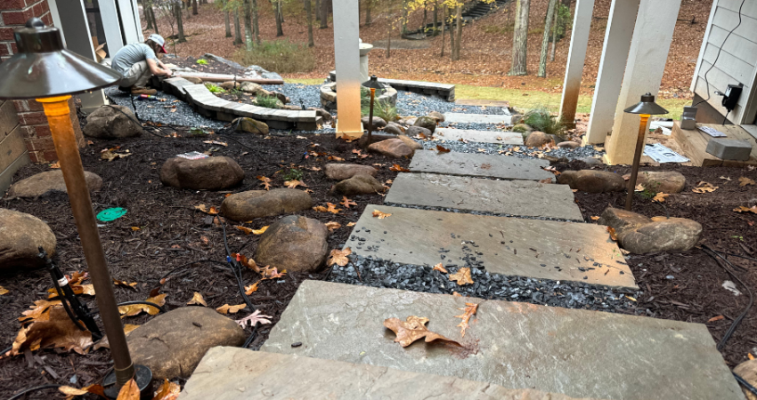 A stone staircase leads down toward a landscaped garden area where a person is working near a retaining wall.