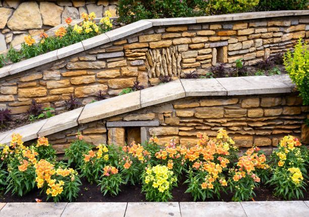 Stacked stone garden walls with tiered flower beds featuring blooming yellow and orange snapdragons.