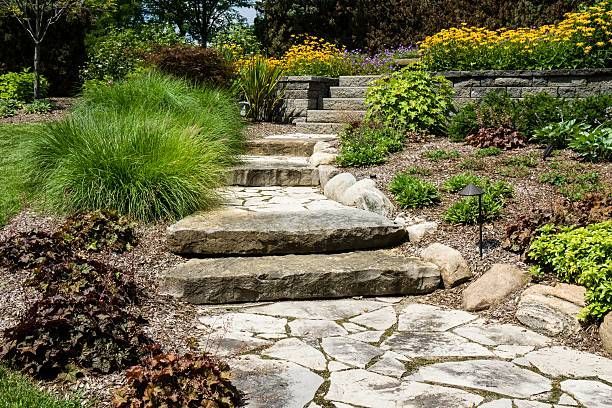 Stone steps and a flagstone path wind through a vibrant garden with ornamental grasses, foliage, and yellow flowers.