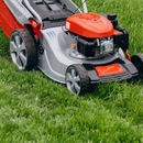 A person mows a bright green lawn with a silver and orange gas-powered lawn mower.