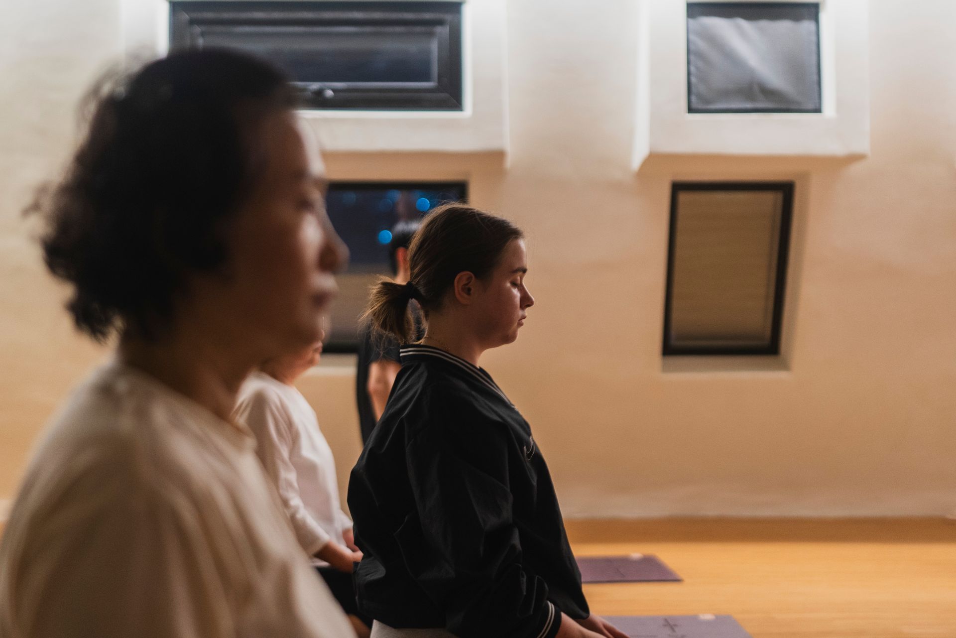 People meditating in a studio with small windows; focus on a woman with eyes closed.