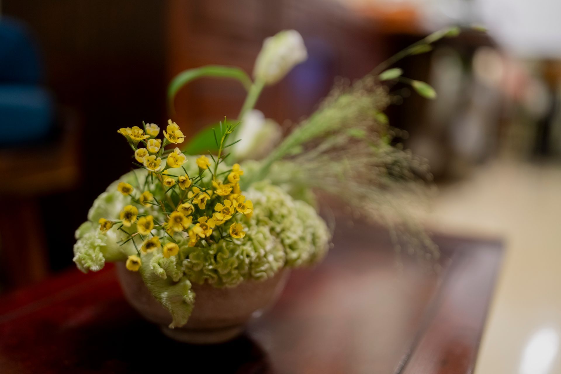 분홍빛 그릇에 담긴 작은 꽃꽂이에는 노란색과 흰색 꽃이 담겨 있으며, 나무 테이블 위에 놓여 있습니다.