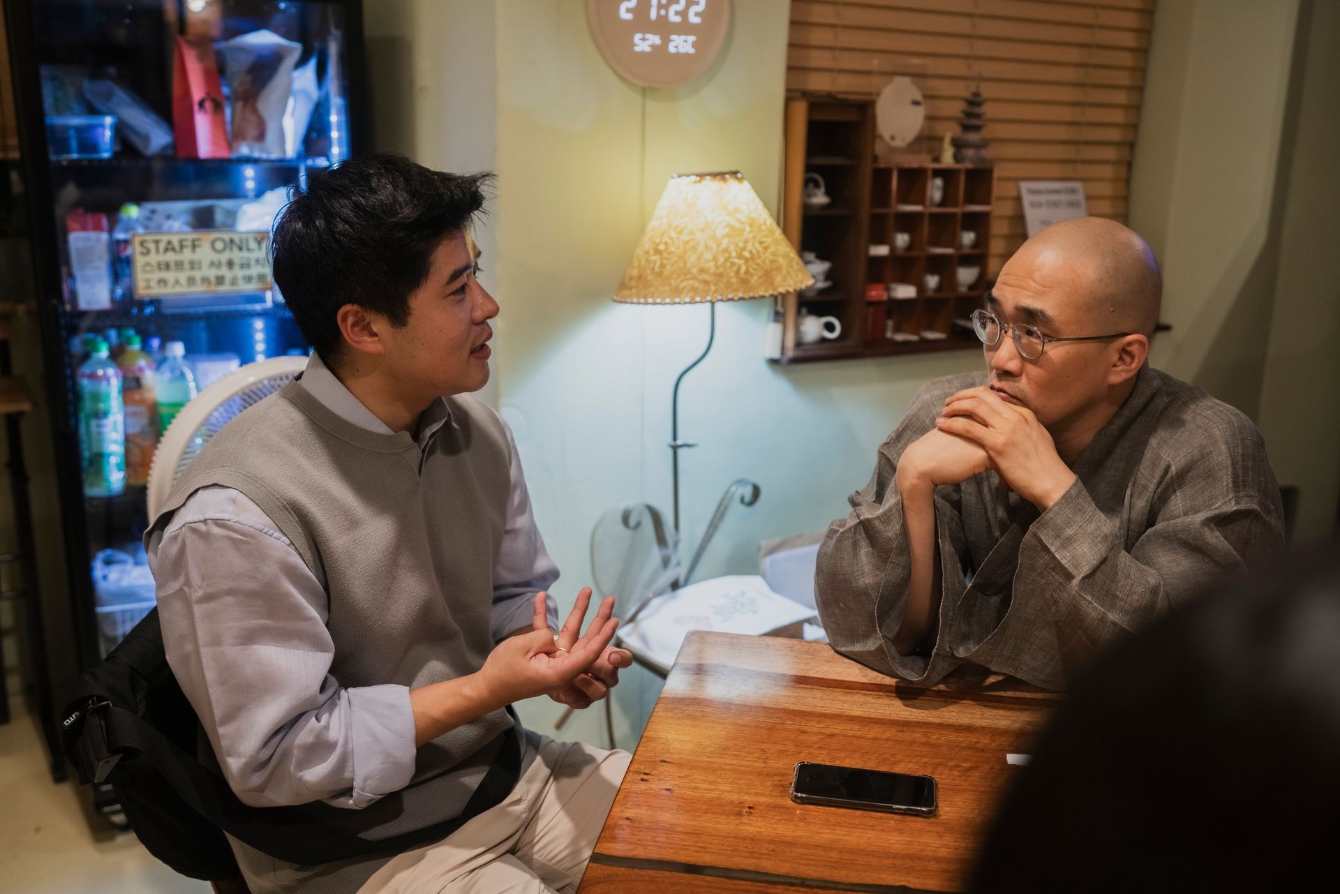 Two men conversing at a table. One gestures, the other listens intently in a cafe setting.