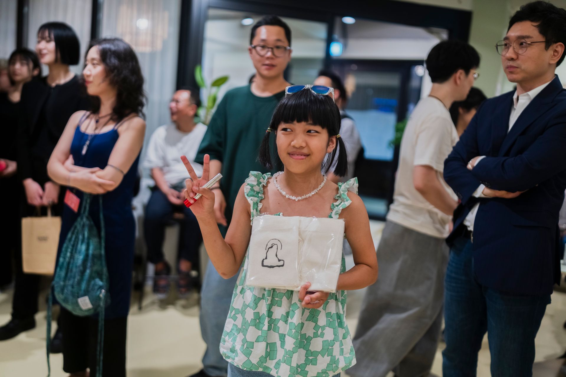 사람들이 있는 방에서 예술 작품과 평화의 표시를 들고 있는 어린 소녀가 미소 짓고 있습니다.