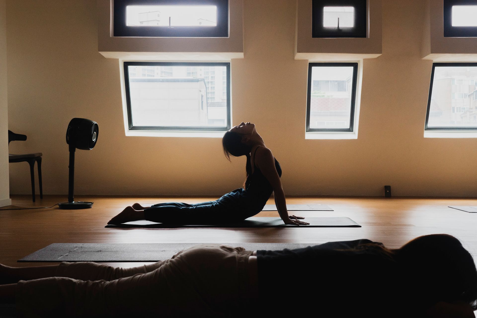 A person in a yoga pose, arched back, in a sunlit studio.