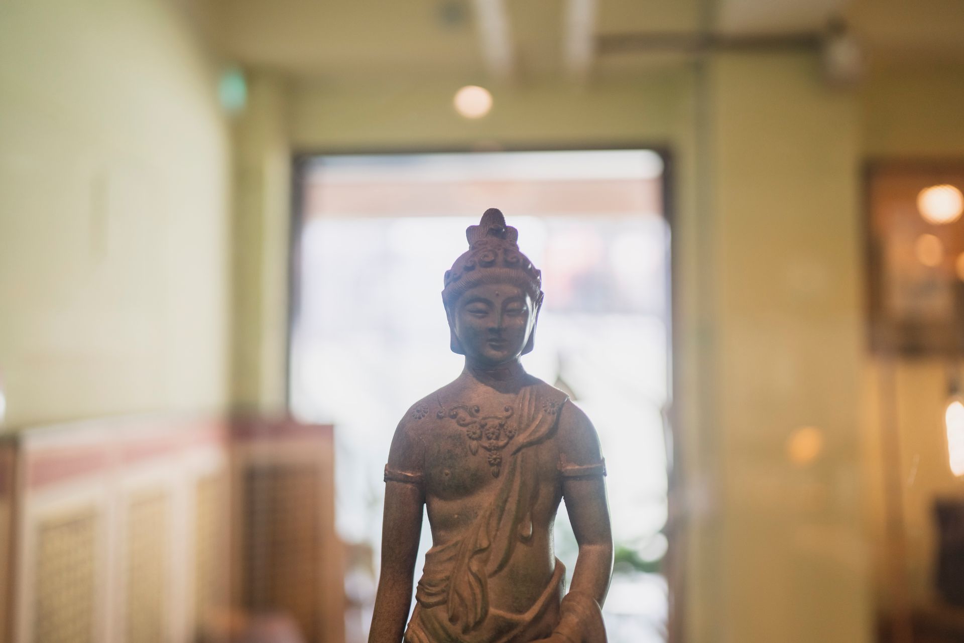 Statue of Buddha in a room; wearing a crown, and draped in cloth. Blurred background.