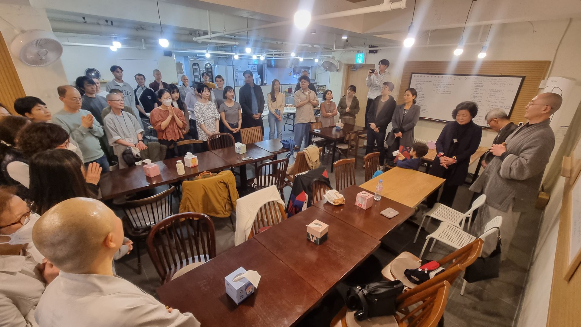 방 안에 있는 사람들, 대부분은 노인들로, 회의나 모임에 참석한 것처럼 보이며, 스님도 그 자리에 있습니다.