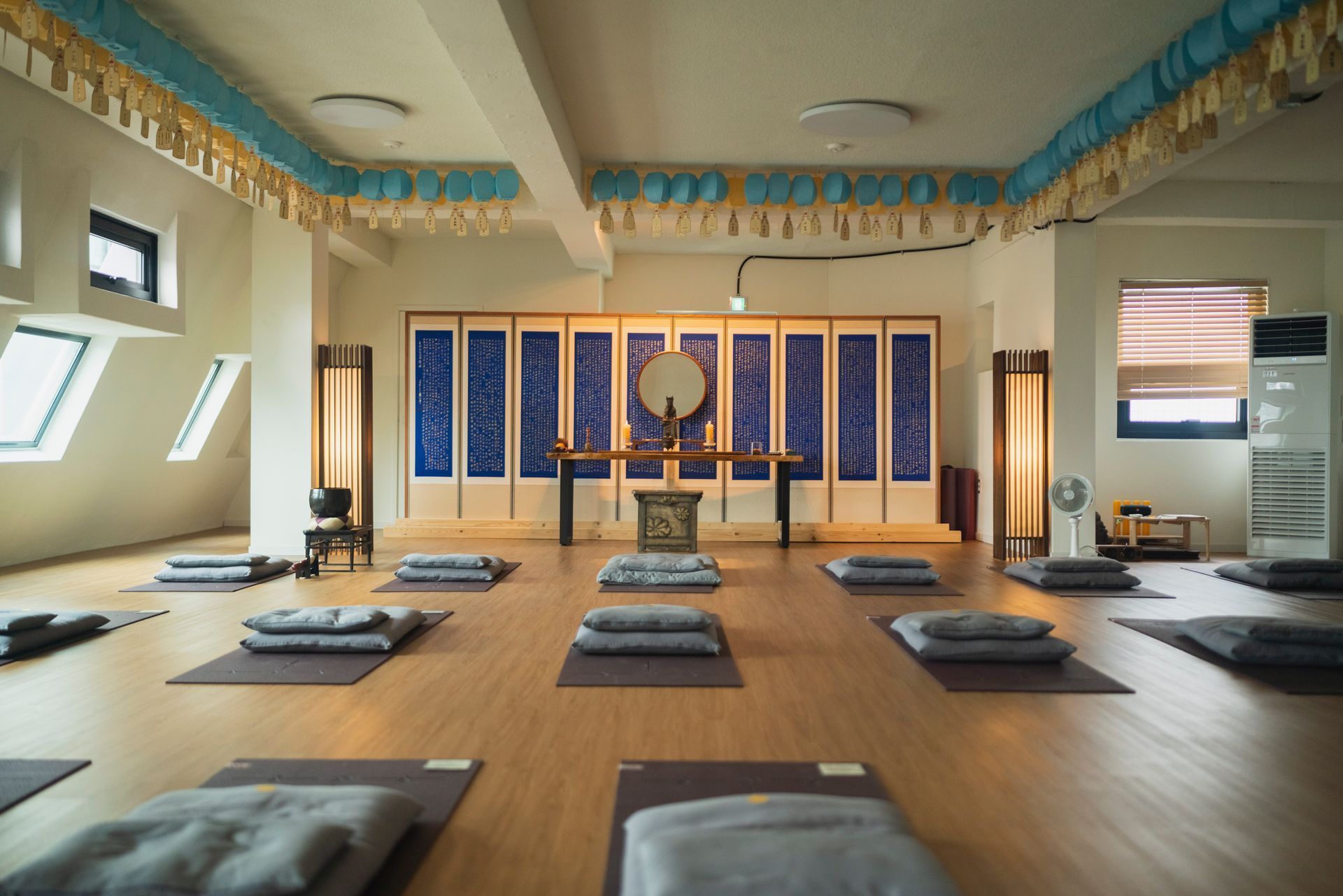Yoga studio with mats and cushions arranged for meditation; a traditional wall with blue and white panels.