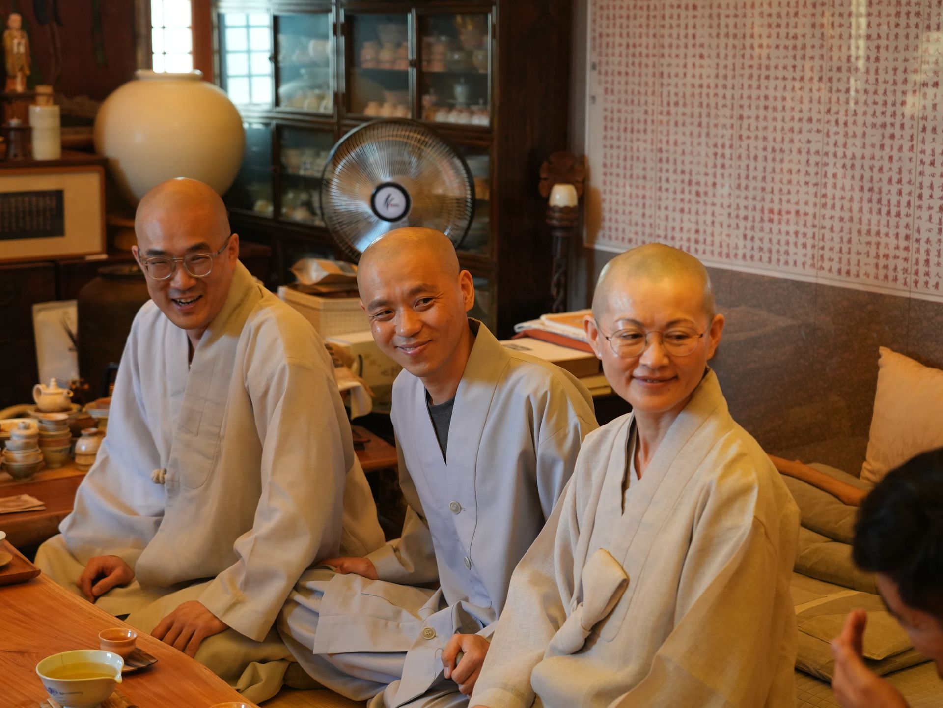 Three smiling Buddhist monks in light robes, indoors.