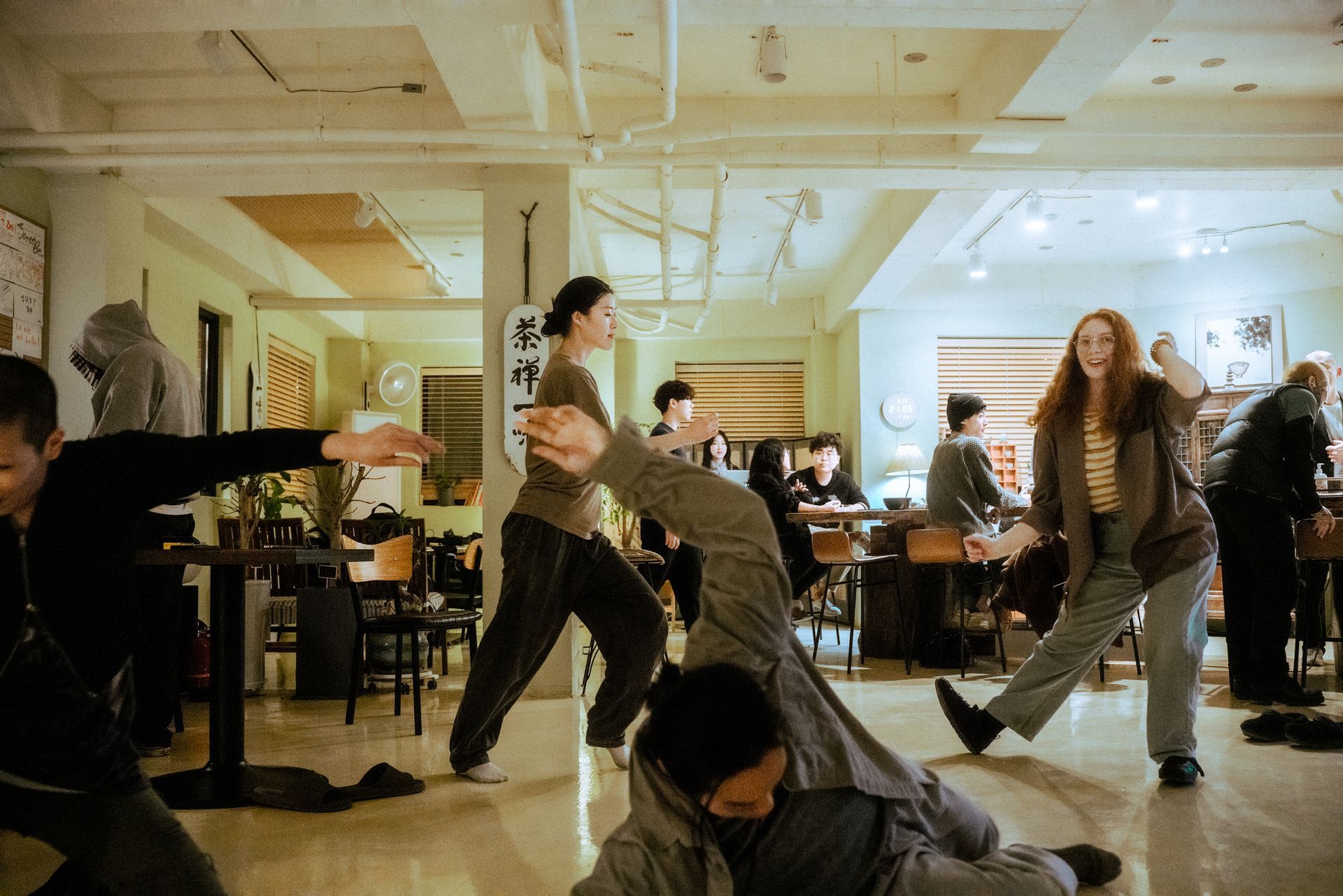 People practicing martial arts inside a cafe. Several in motion, focused expressions, neutral color palette.