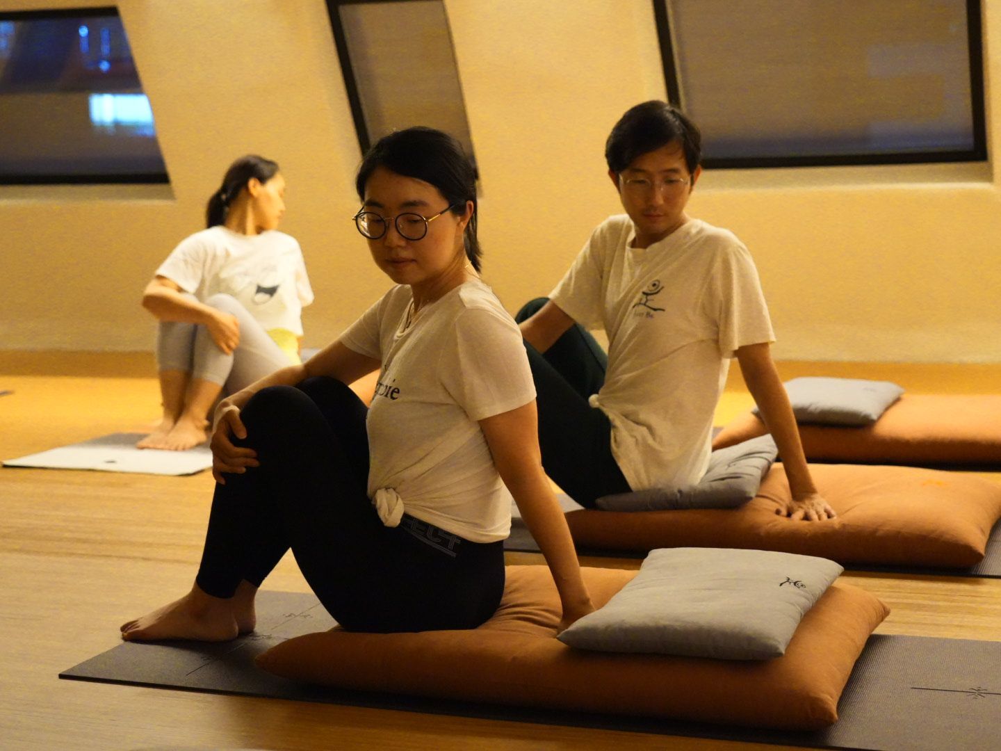 Three people doing a seated yoga twist in a studio, using cushions.