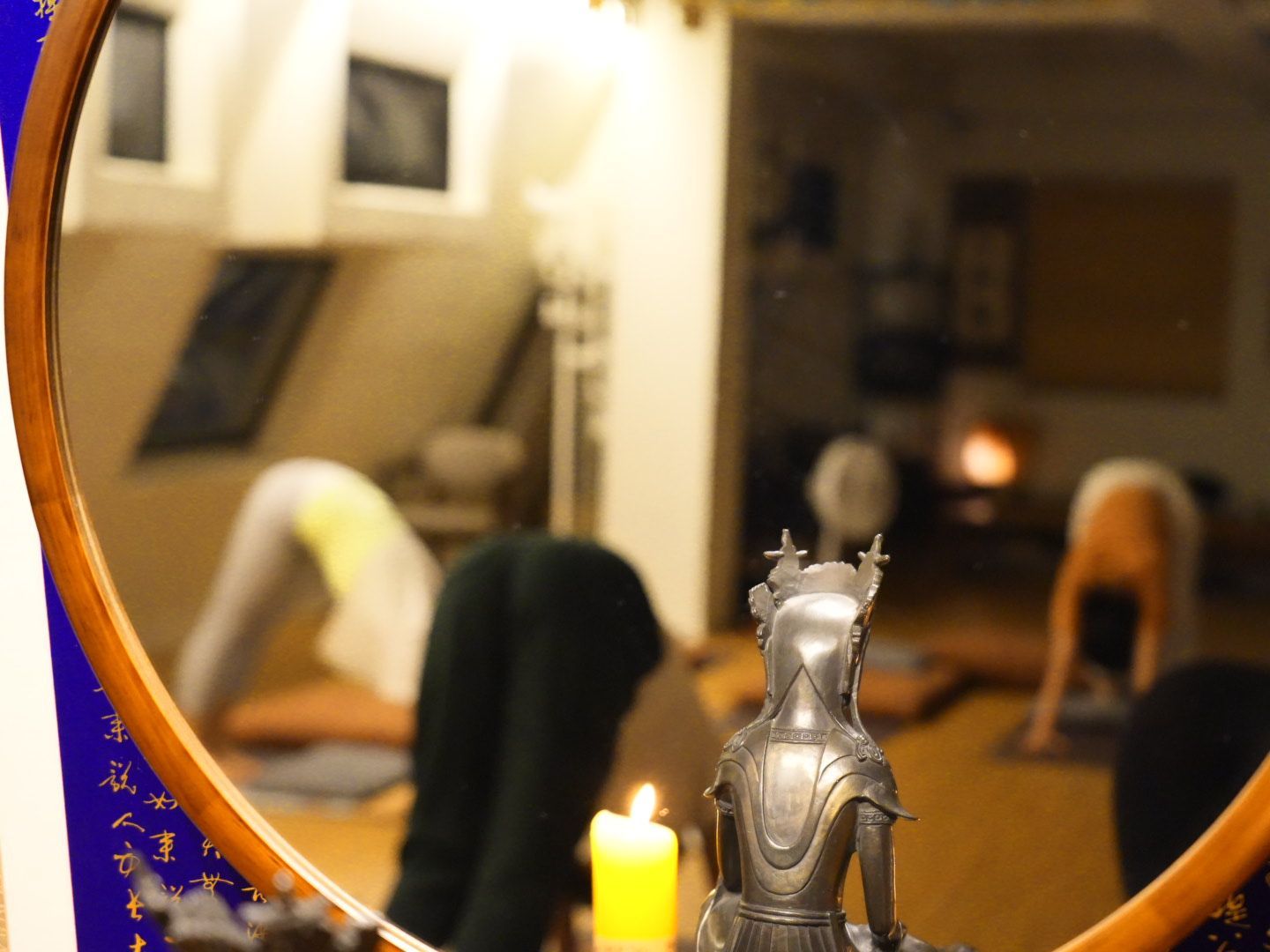 Mirror reflecting people in yoga pose, candle, statue in an indoor studio setting.