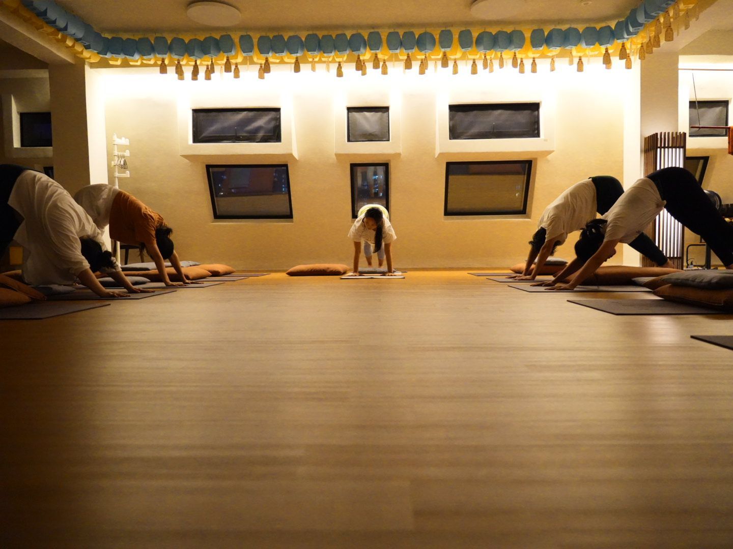 People doing yoga in a studio. Instructor in the center, participants in Downward-Facing Dog pose.