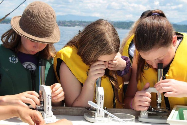 3 girls wearing life jackets looking through a microscope