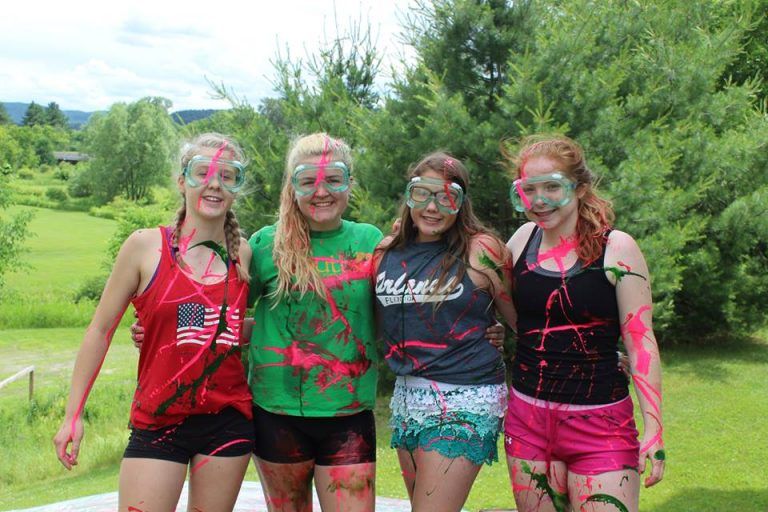 4 girls standing together wearing goggles and covered in paint