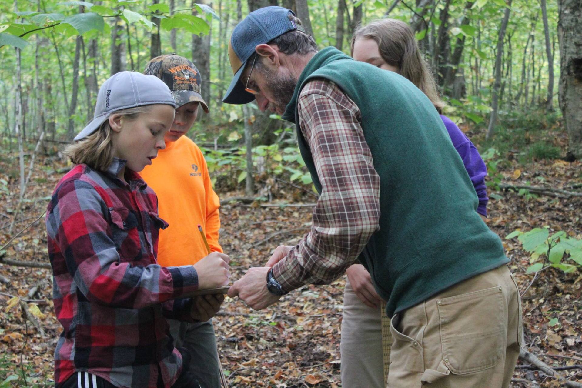 teacher teaching three students about nature in the woods