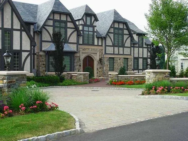 Tudor-style house with stone and dark wood accents; landscaped front yard with a circular driveway.
