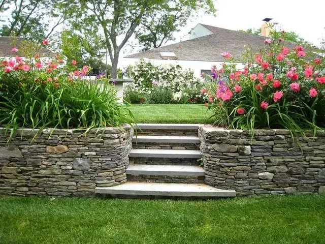 Stone steps lead up to a garden with pink flowers and green grass.