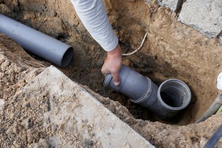 A person is holding a pipe in a hole in the ground.