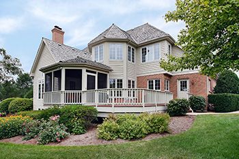 Back view of a two-story house with a screened porch, deck, and brick exterior, surrounded by landscaping and green grass.