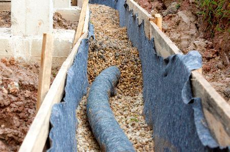 A pipe is being installed in a trench filled with gravel.