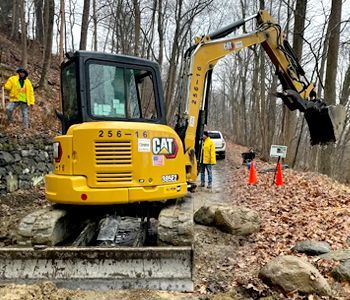 A yellow cat excavator is sitting on a dirt road in the woods.