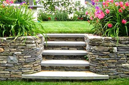 A stone wall with stairs leading up to a garden with flowers.