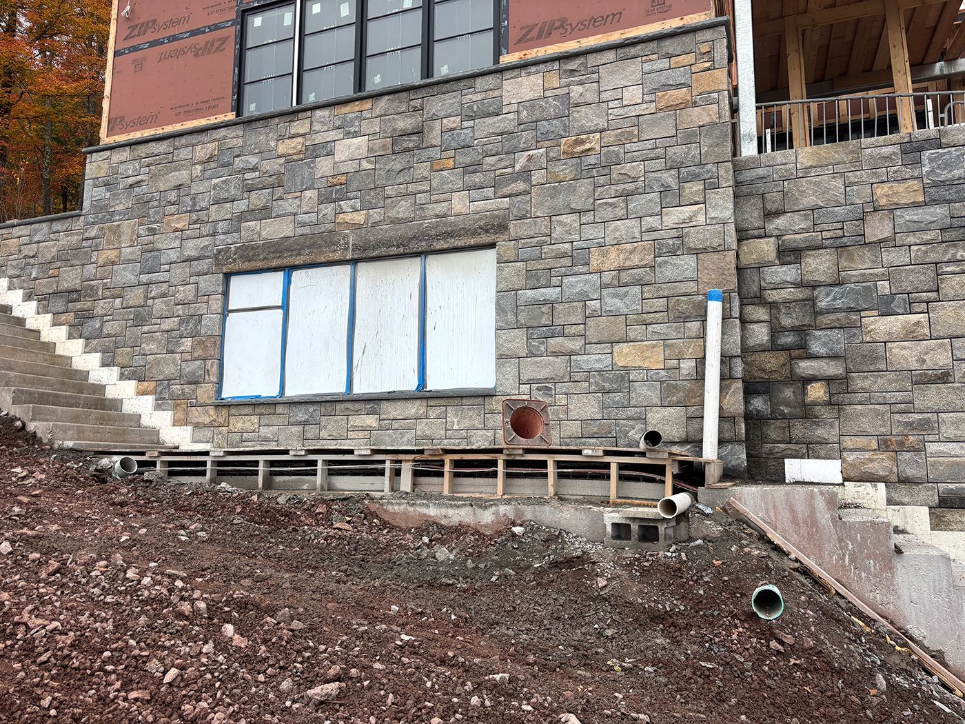 Stone-walled building under construction on a hillside. Wooden framework, windows covered in blue tape.