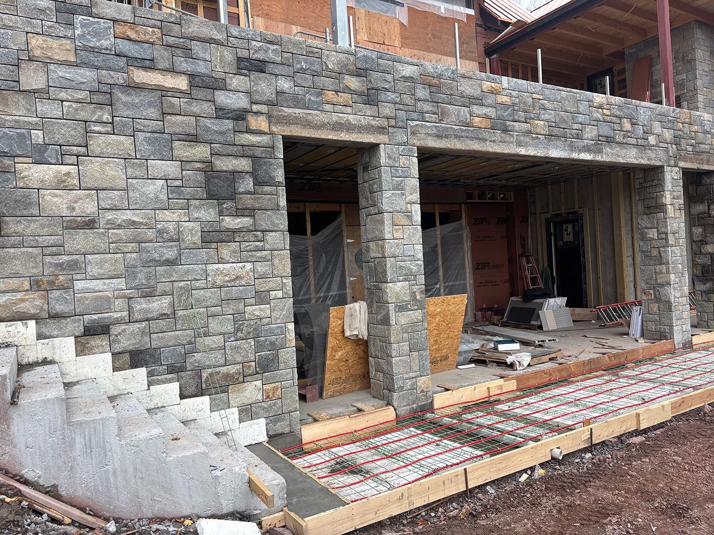 Stone building exterior under construction with exposed doorways and concrete stairs.