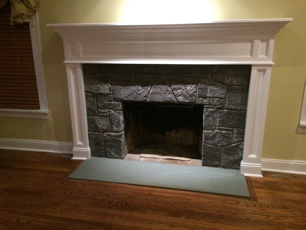 Fireplace with gray stone facade, white mantel, and green hearth, in a room with wood floors and blinds.