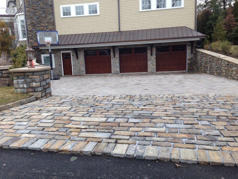 Driveway paved with stone leading to a three-car garage with brown doors, set against a beige house.