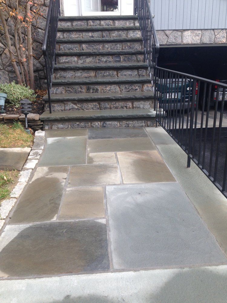 Stone walkway leading to steps with black iron railings; gray house in background.