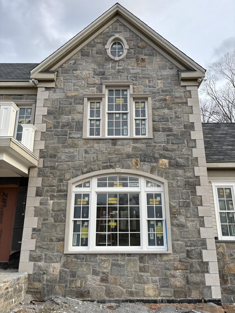 Stone facade of a house with several white-framed windows, beige trim, and a dark roof.
