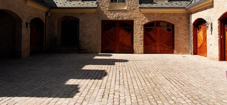 A cobblestone driveway in front of a building with multiple arched wooden doors and shadows.
