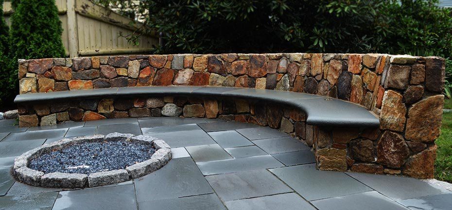 Stone bench curved around a fire pit, on a patio.